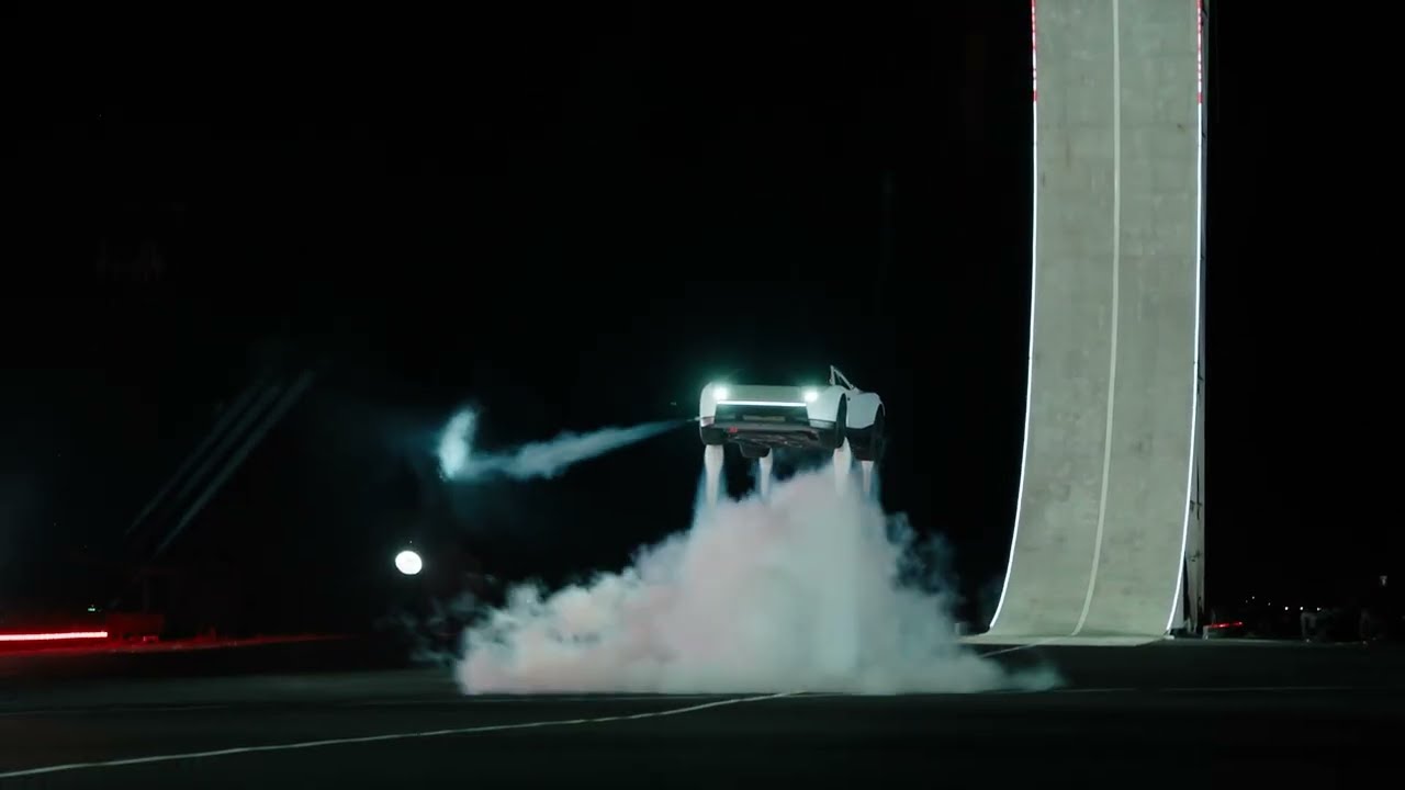 El Tesla Roadster blanco suspendido en el aire, de noche, sostenido por cuatro chorros de gas frío, frente a una rampa curva iluminada.