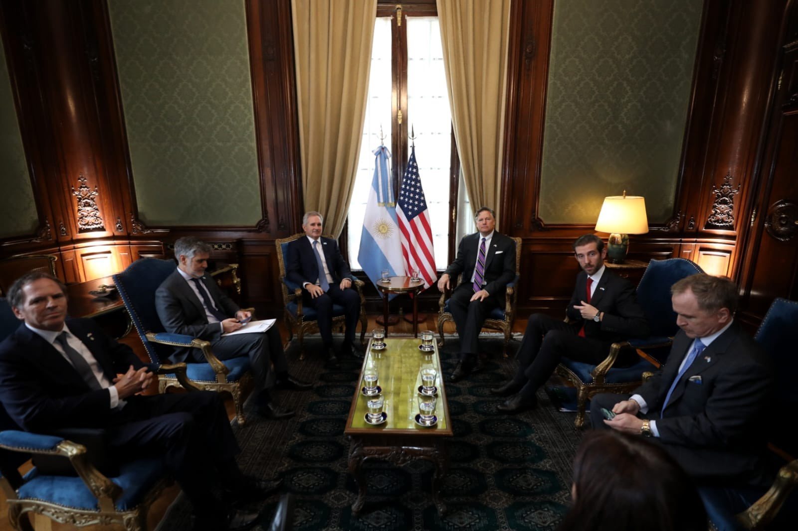 Las delegaciones de la Argentina y de los Estados Unidos sentadas en un salón del Palacio San Martín, con Quirno y Landau en el centro junto a las dos banderas