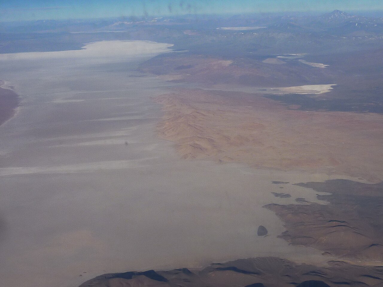 Vista aérea del salar de Arizaro, una extensa llanura de sal blanquecina entre cerros rojizos de la Puna, con cordones montañosos al fondo