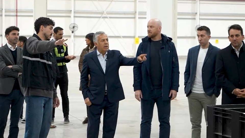 El gobernador Alfredo Cornejo, de traje oscuro, señala hacia el interior de un galpón logístico mientras recorre el centro de Mercado Libre en Luján de Cuyo junto a directivos y funcionarios