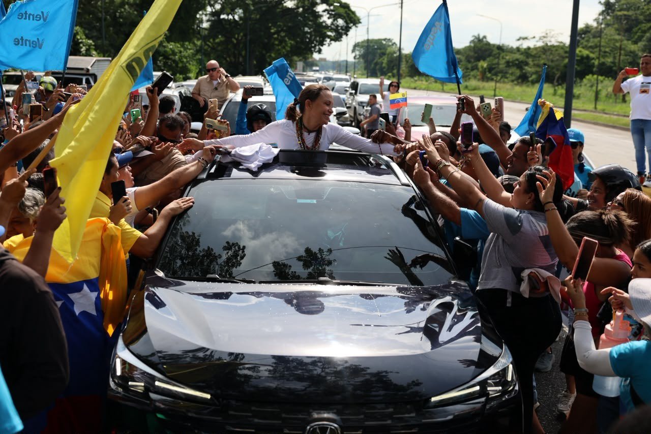 María Corina Machado, asomada por el techo de un auto, saluda a simpatizantes con banderas de Venezuela y de Vente Venezuela en una ruta del estado Yaracuy