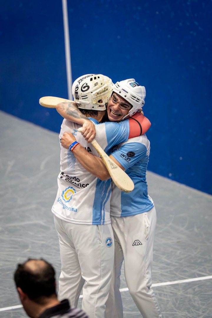 Dos paletistas argentinos con casco se abrazan en la cancha tras ganar un punto