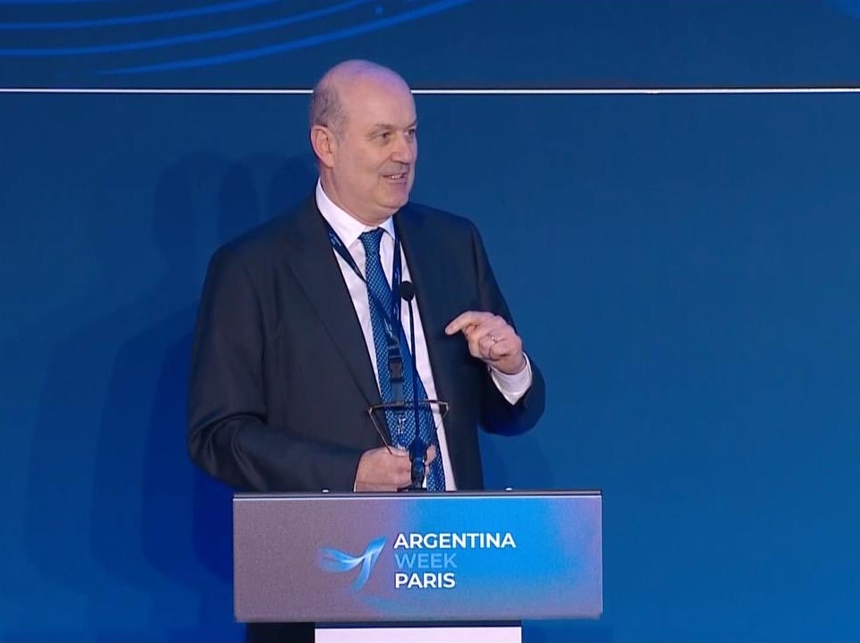 Federico Sturzenegger habla de pie detrás de un atril con el logo de Argentina Week Paris, frente a una pantalla azul