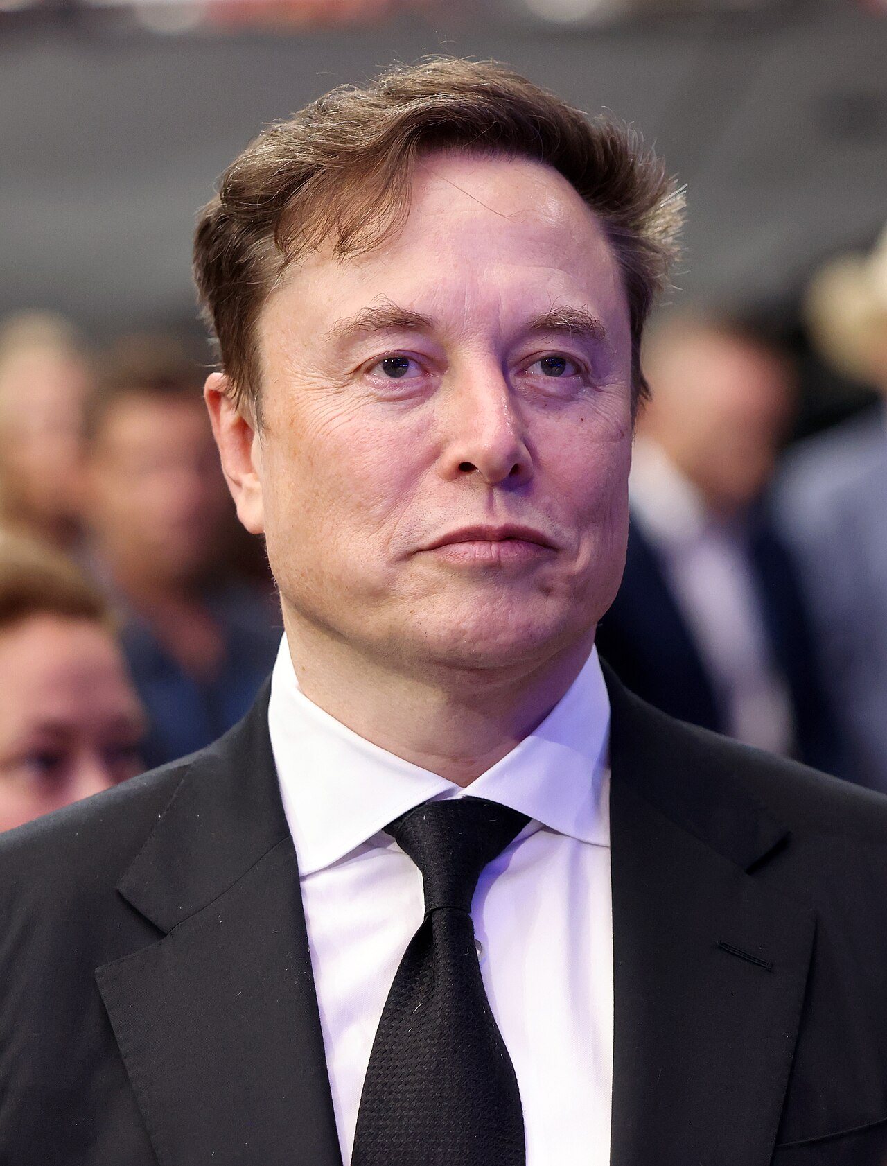 Elon Musk, de traje oscuro, en un acto en un estadio.