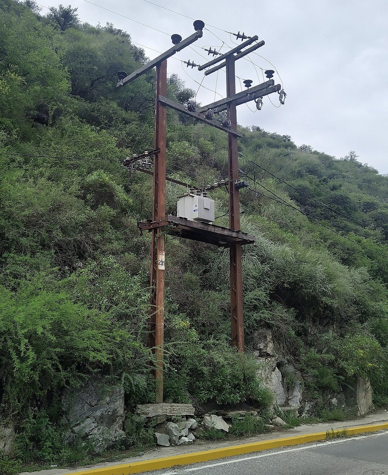 Postes de acero con un transformador y cables de distribución eléctrica en una calle de San Roque, Córdoba.