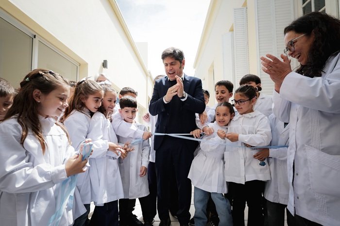 Axel Kicillof aplaude junto a alumnos de guardapolvo blanco que sostienen una cinta celeste en el corte inaugural de la escuela