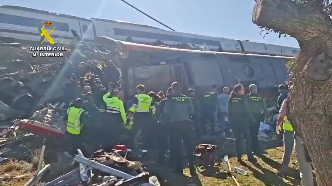Agentes de la Guardia Civil y rescatistas con chalecos amarillos junto a un vagón volcado, entre restos metálicos