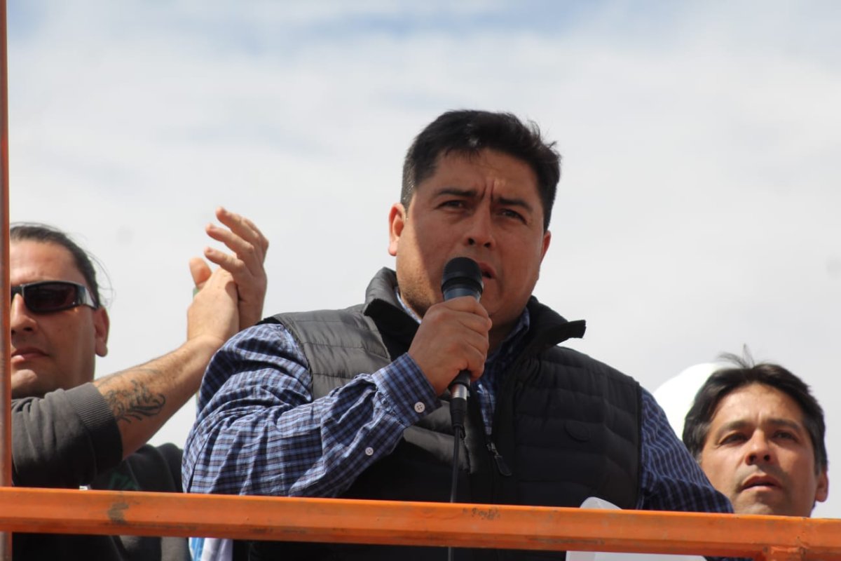 Claudio Vidal habla con un micrófono desde una plataforma, con trabajadores detrás.